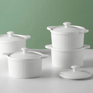 Set of white ceramic containers with lids on a light gray surface against a green background