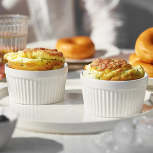 Two soufflés in white ramekins on a table with donuts in the background.