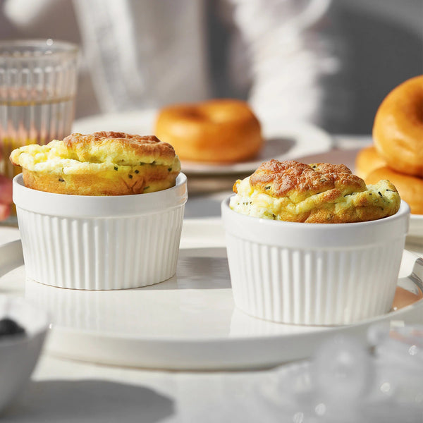 Two soufflés in white ramekins on a table with donuts in the background.