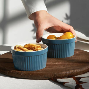 Two blue ramekins on a wooden surface with a hand reaching for one of them.