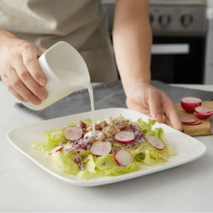 Person pouring dressing onto a salad on a white plate in a kitchen setting.