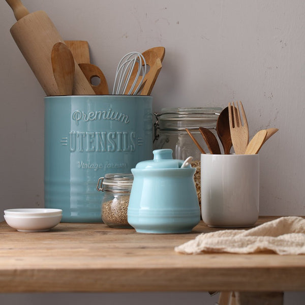 Kitchen utensils and containers on a wooden table with a neutral background