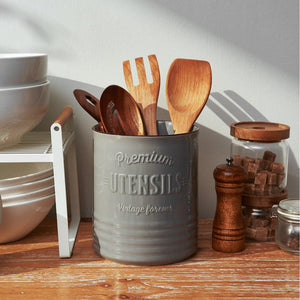 Gray container with wooden utensils on a wooden surface with kitchen items in the background