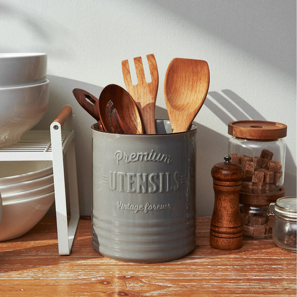 Gray container with wooden utensils on a wooden surface with kitchen items in the background