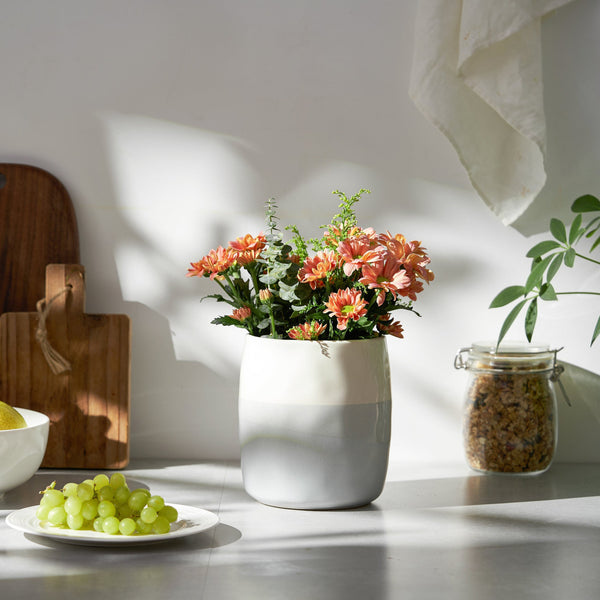 blue and white utensil crock with flowers on a table with a plate of grapes and a jar in the background.