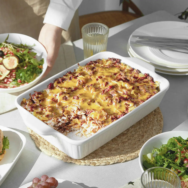 Baked dish in a white casserole dish on a dining table with plates and salad.