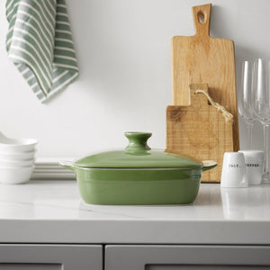 Green ceramic baking dish on a kitchen counter with cutting board and utensils in the background
