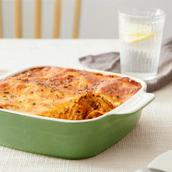 Baked dish in a green casserole dish on a table with a glass of water in the background.
