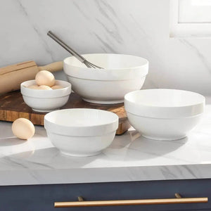 Set of white ceramic bowls on a kitchen counter with a rolling pin and eggs.