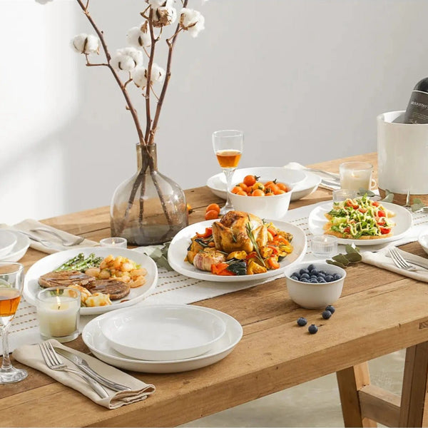 ceramic serving dishes with plates of food, glasses, and a vase with cotton branches.
