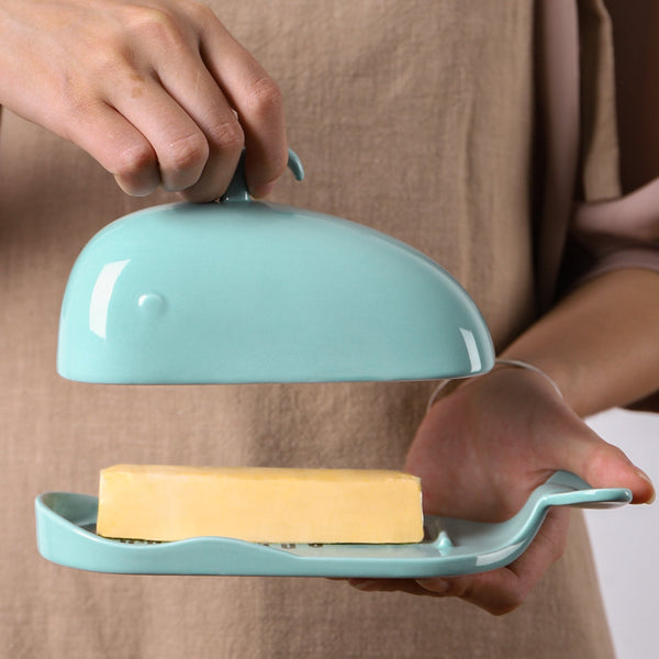 Person holding a turquoise butter dish with a block of butter inside