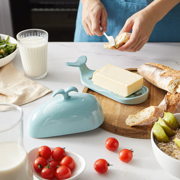 Butter dish shaped like a whale on a table with bread, tomatoes, and milk.