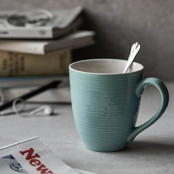 Turquoise coffee mug with a spoon on a table with newspapers in the background