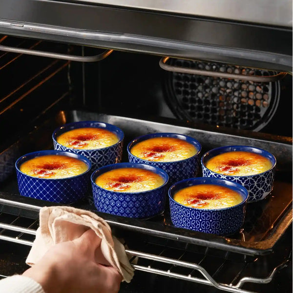 Person placing blue ramekins with custard into an oven