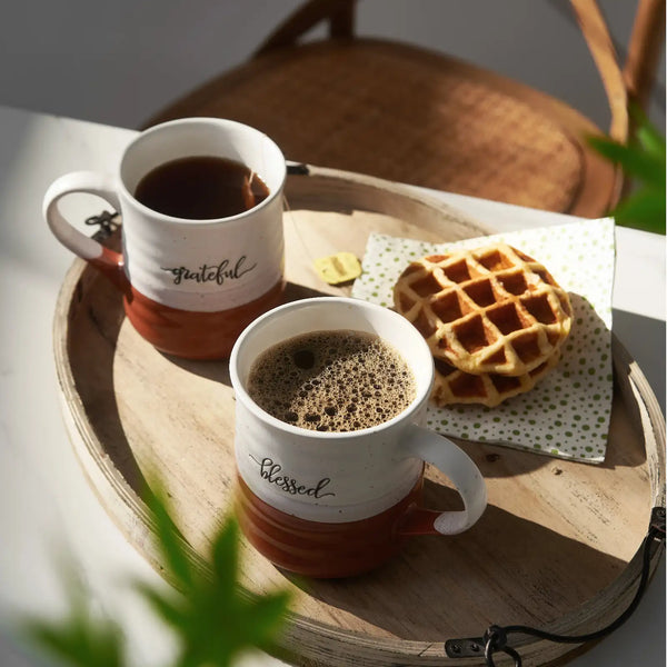 Two orange and white mugs with coffee and waffles on a wooden tray