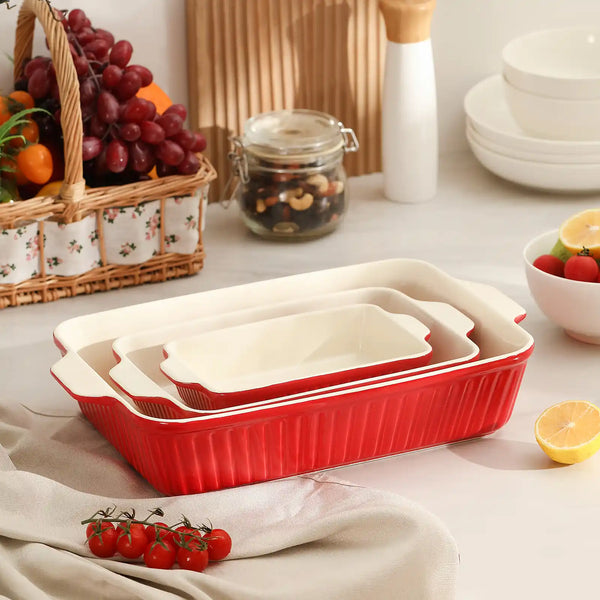 Set of red ceramic baking dishes on a kitchen counter with fruits and vegetables.