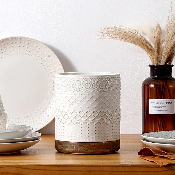 White textured kitchen utensil holder on a wooden surface with decorative elements.