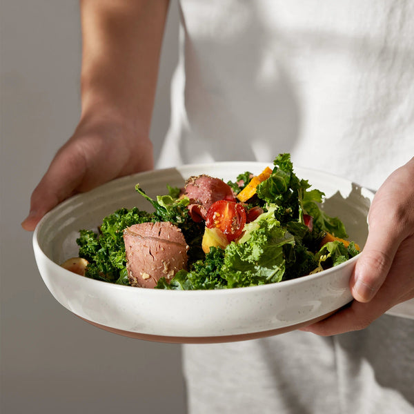 Person holding a bowl of salad with greens and meat.