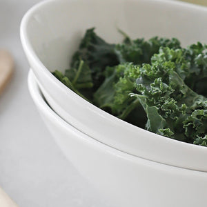 Green leafy vegetables in a white ceramic bowl on a light background