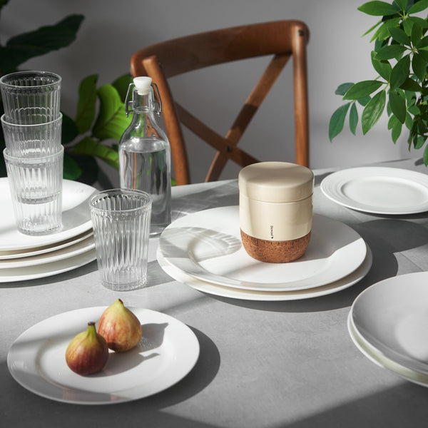 Dining table setting with plates, glasses, a bottle, and a small container on a gray surface.
