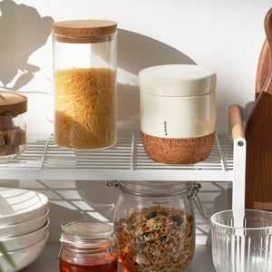 Kitchen shelves with jars containing food items and a white container with cork base.