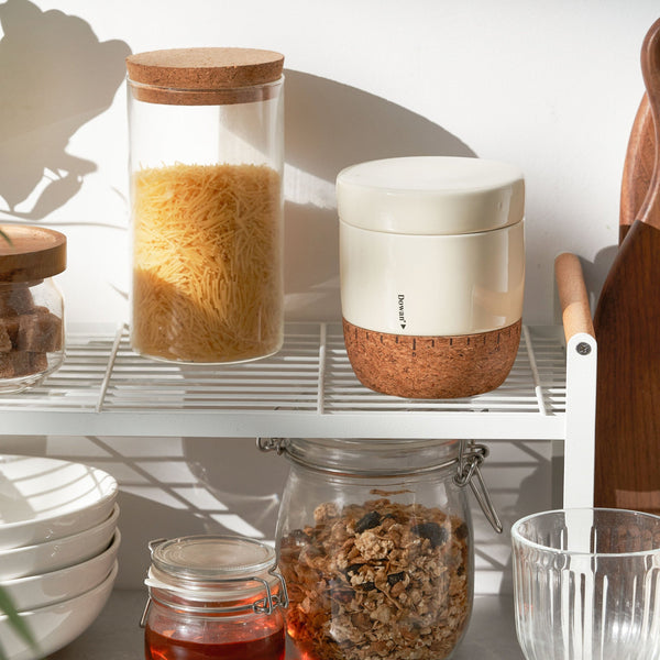 Kitchen shelves with jars containing food items and a white container with cork base.