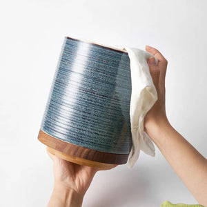 Person cleaning a blue ceramic lamp with a white cloth on a white background