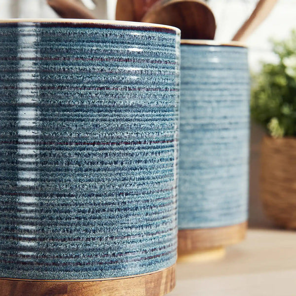 Two blue ceramic planters with wooden bases on a blurred natural background